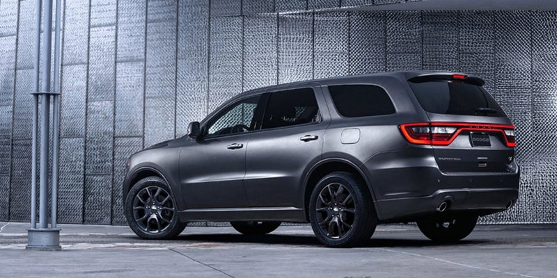 Dark gray SUV with tinted windows parked by a textured concrete wall, viewed from the rear passenger side.