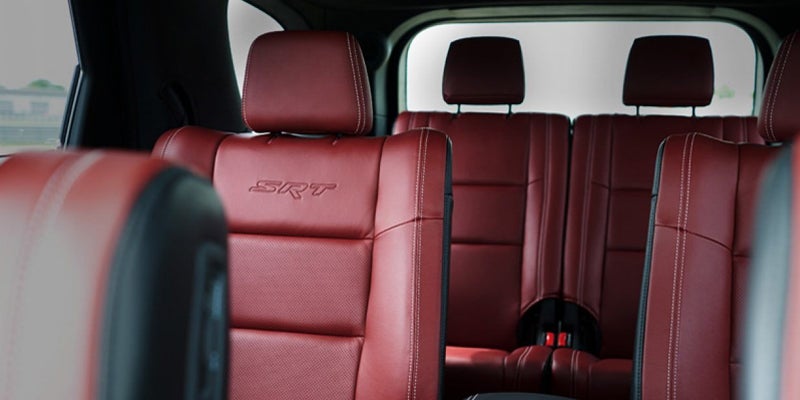 Rows of deep red leather car seats with white stitching, the "SRT" logo embossed on the headrest of a seat.