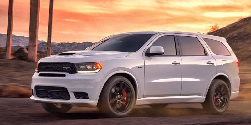 A white Dodge Durango SUV with dark rims speeds past concrete columns at sunset.