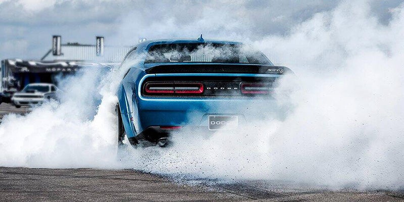 Rear view of a blue Dodge Challenger SRT Hellcat drifting, creating a large cloud of white smoke.