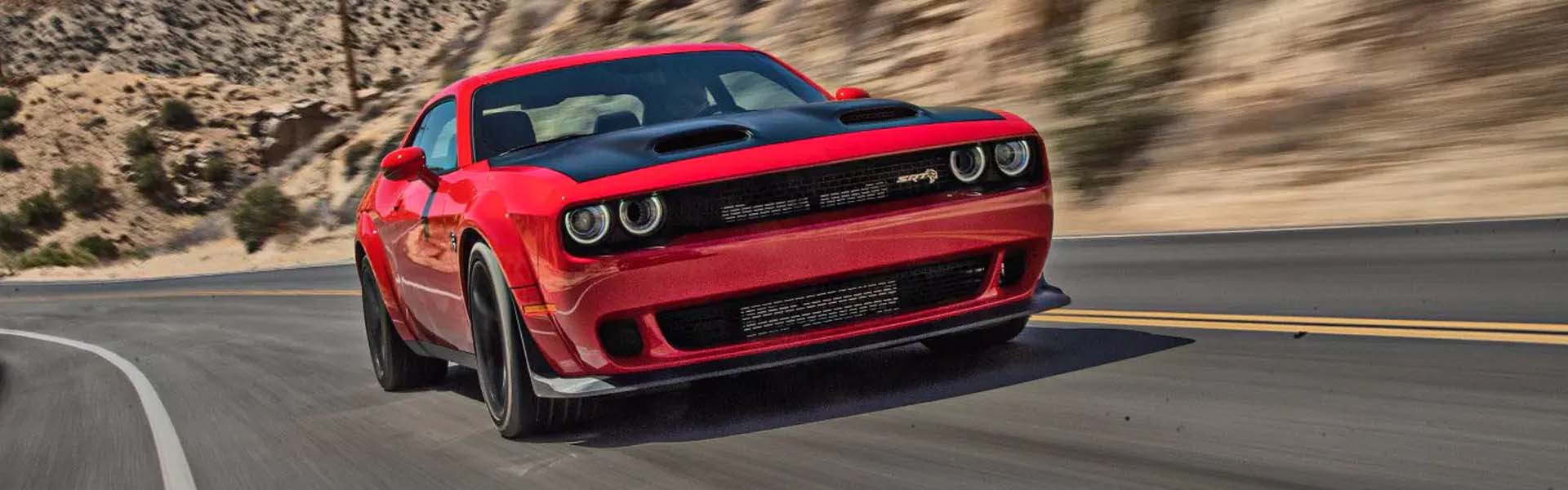A red Dodge muscle car with a black hood speeding around a desert curve.