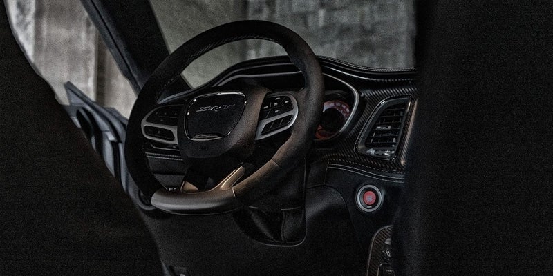 Interior view of a dark sports car, showing the steering wheel with "SRT" logo and a red push-to-start button.