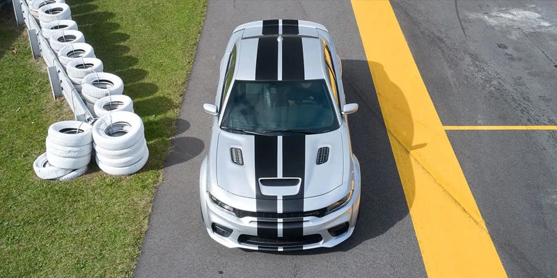 Overhead view of a silver Dodge Charger with two black racing stripes on a racetrack.