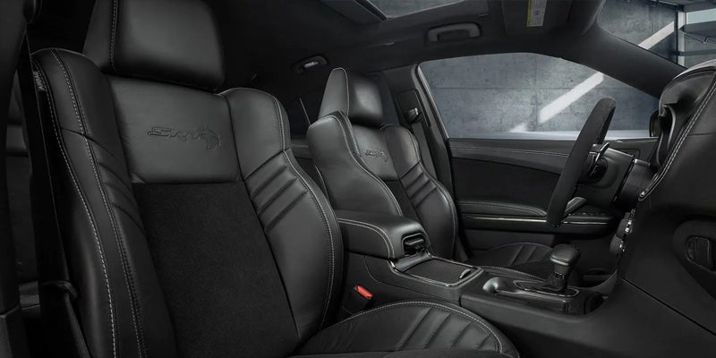 Interior close-up of a car, showing the black leather front passenger and driver seats with white stitching and SRT logos.