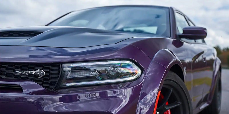 Front-facing view of a shiny purple Dodge Charger SRT with a black hood scoop and bright LED headlights.