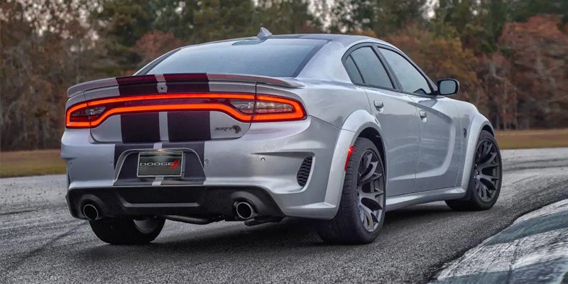 Rear view of a silver Dodge Charger with two black racing stripes, on a race track.