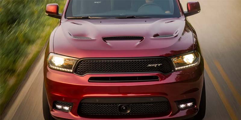Front view of a shiny, maroon Dodge Durango SRT on the road, with headlights and fog lamps illuminated.