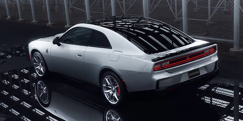 Silver Dodge Challenger Concept with a black roof and red taillights, parked on a reflective black surface.