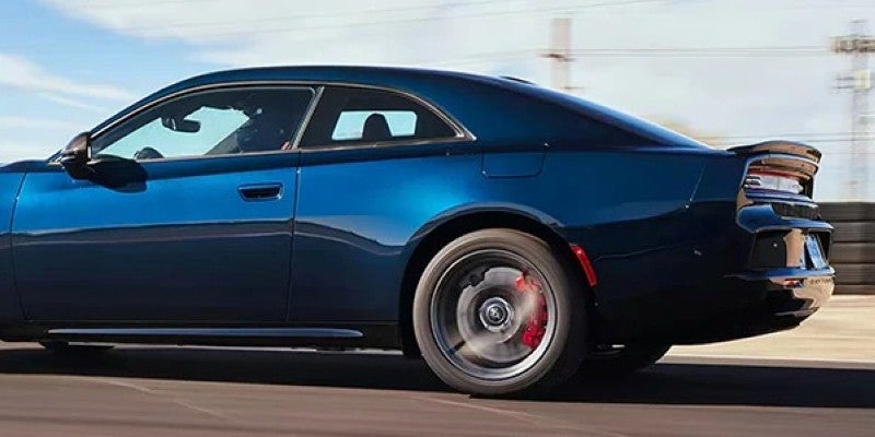 Rear three-quarter view of a dark blue sports car with red brake calipers visible through the spinning wheel.