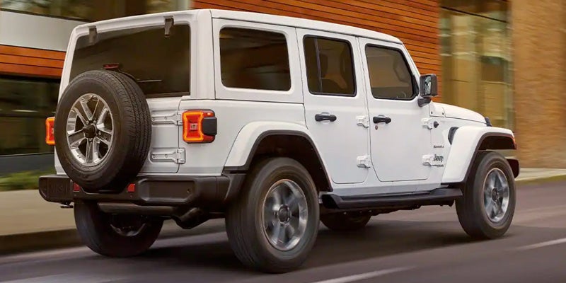 Rear view of a white Jeep Wrangler driving on a paved road next to a modern building.