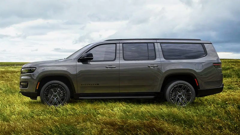 A gray Wagoneer SUV parked sideways in a grassy field under a cloudy sky.
