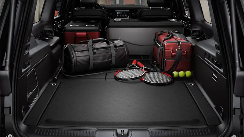 VIEW OF A BLACK JEEP SUV TRUNK WITH DUFFEL BAGS, COOLERS, TENNIS RACKETS, AND TENNIS BALLS.
