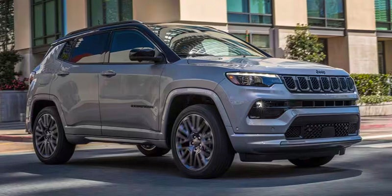 Light gray Jeep Compass SUV with a black roof, driving on a city street.