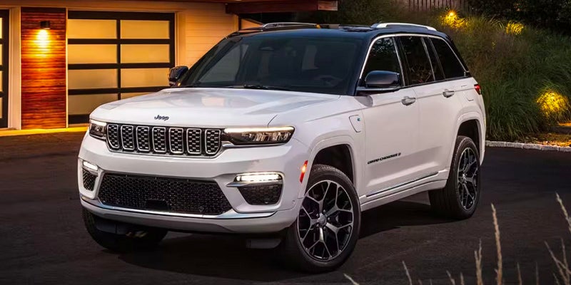 A white Jeep Grand Cherokee Laredo 4xe SUV with a black roof parked in a driveway at dusk.