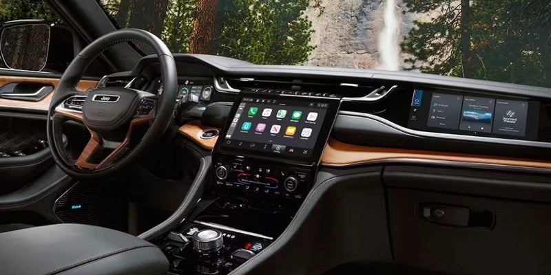The interior of a vehicle featuring a large central touchscreen and a smaller display for the passenger, with a waterfall in the background.