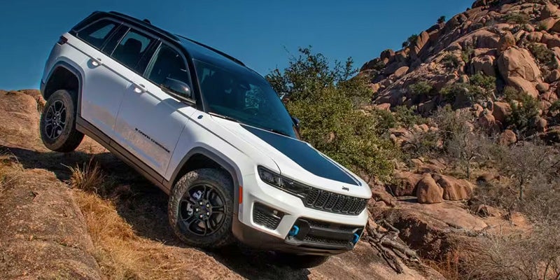 A white Jeep Grand Cherokee, with a black roof and hood accent, angled uphill on a rocky off-road trail