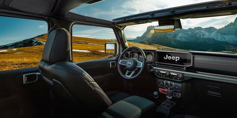 Interior view of a Jeep with top panels removed, showing front seats, steering wheel, dashboard, and mountain landscape.