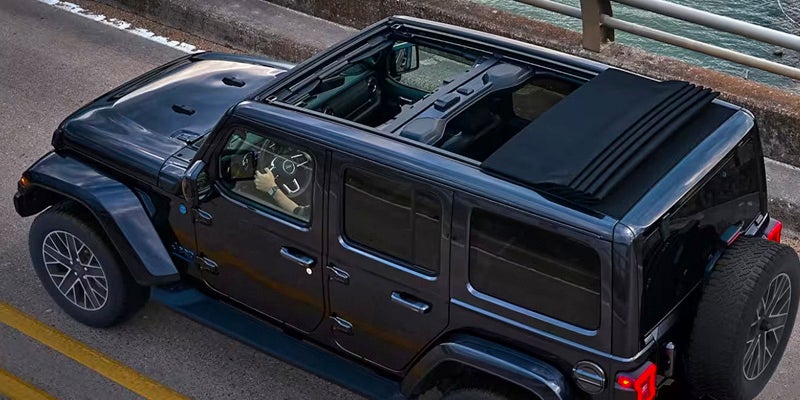Overhead view of a black Jeep with its soft top partially retracted, revealing the interior cabin.