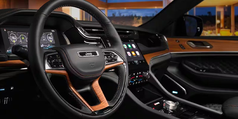 Luxurious car interior featuring a black leather steering wheel with wood accents, large digital displays, and wood trim.