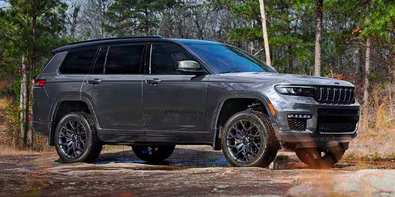 Dark grey 2023 Jeep Grand Cherokee L parked on a muddy path in a wooded area.