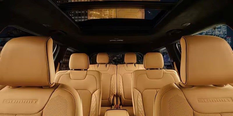 Three rows of tan leather car seats with "SUMMIT" embossed on the headrest, a city view through the sunroof.