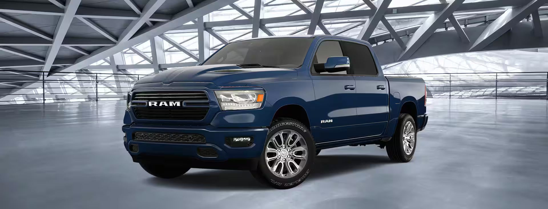 A dark blue Ram 1500 truck with chrome wheels is parked on a light grey floor in a modern, open-ceiling building.