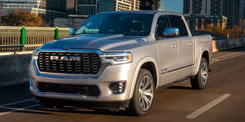 A silver Ram pickup truck on a highway, with city buildings blurred in the background.