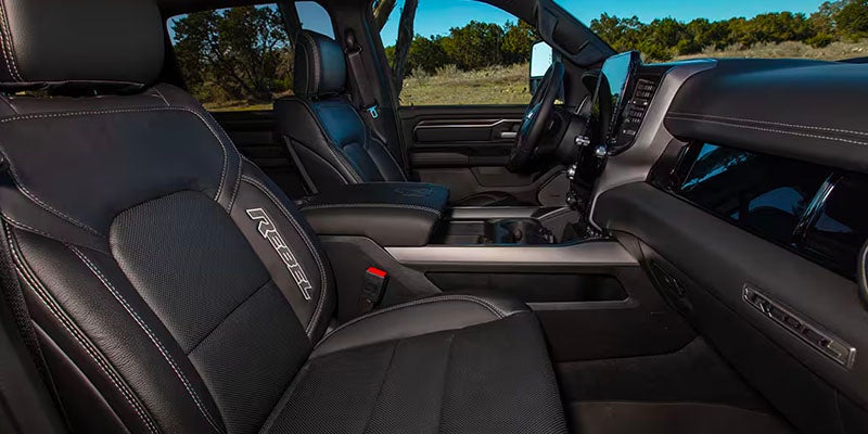 Front interior view of a Ram Rebel pickup truck, showing two black leather seats with white stitching and the "REBEL" logo.