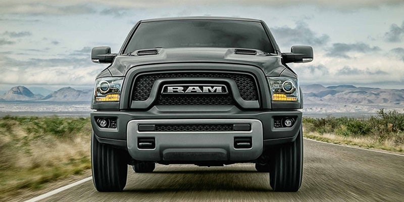 Front view of a dark grey Ram pickup truck on a desert road, mountains in the distance.